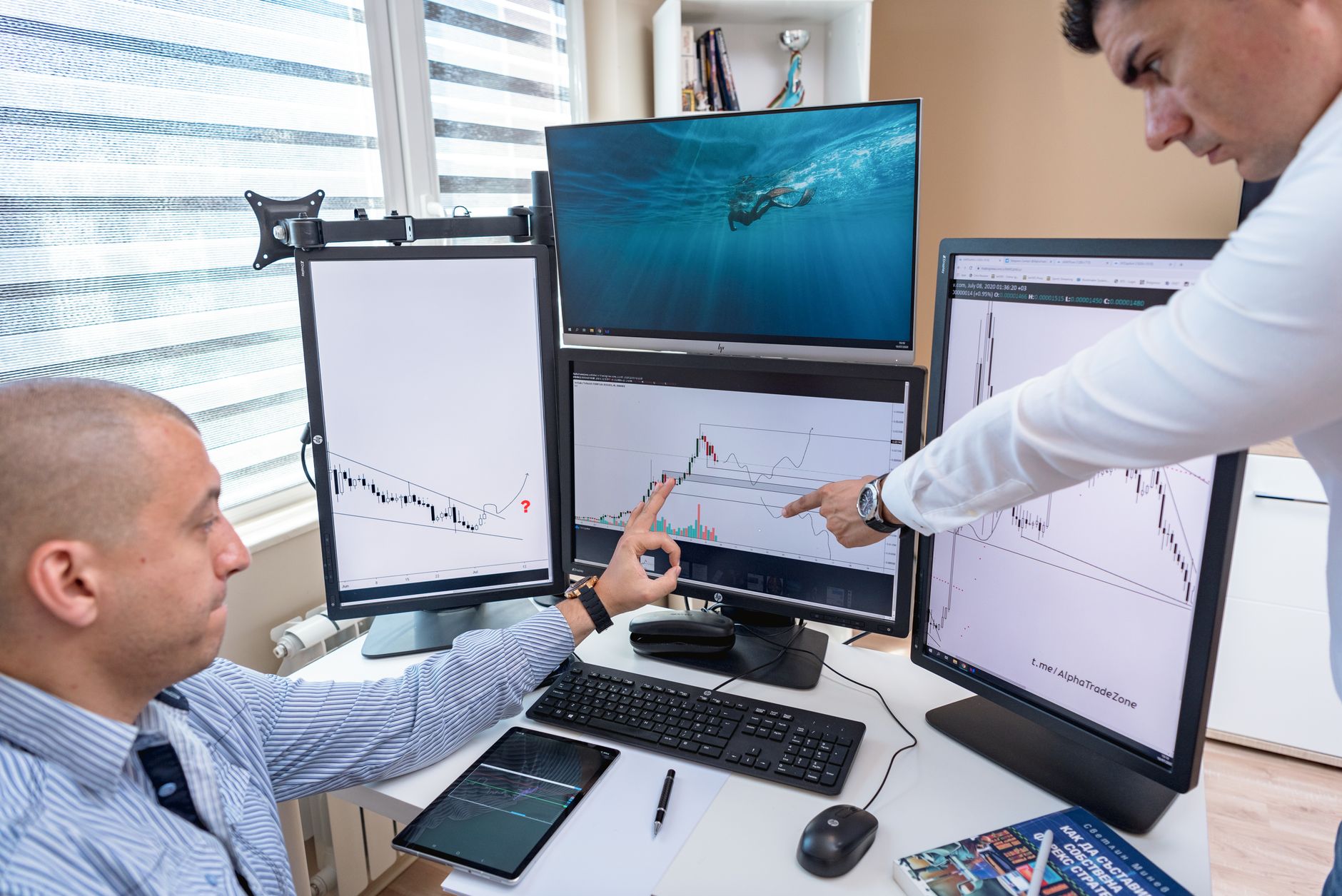 Two operators reading live campaign numbers across several screens in a dim workspace.